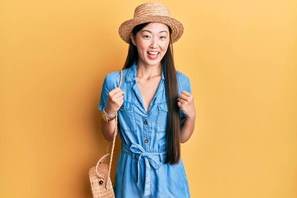 Fiatal kínai nő visel nyári kalap ünneplő meglepett és csodálkozott a siker karok felemelt és nyitott szemmel. győztes koncepció.  - Fotó, kép