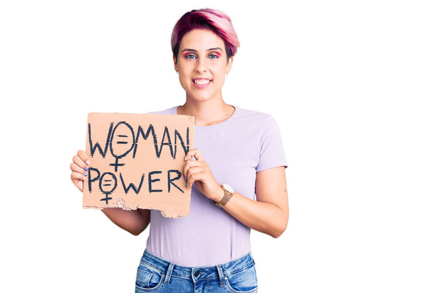 Young beautiful woman with pink hair holding woman power banner looking positive and happy standing and smiling with a confident smile showing teeth  - Photo, Image
