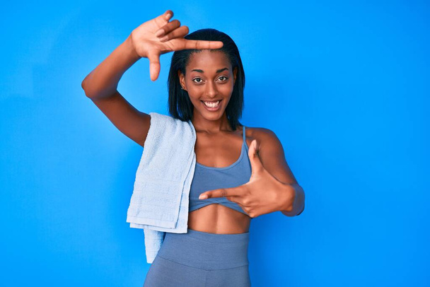Jeune femme afro-américaine portant des vêtements de sport souriant faisant cadre avec les mains et les doigts avec le visage heureux. concept de créativité et photographie.  - Photo, image