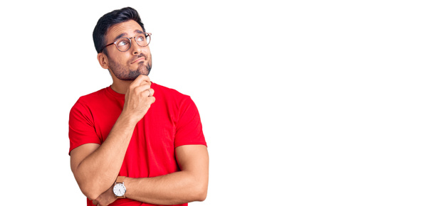Young hispanic man wearing casual clothes and glasses serious face thinking about question with hand on chin, thoughtful about confusing idea  - Fotó, kép