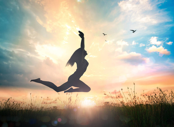 Conceito de bem-estar: Silhueta de mulher feliz pulando com as mãos levantadas em laranja outono natureza pôr-do-sol fundo - Foto, Imagem