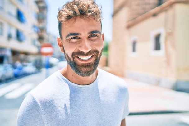 Genç İspanyol adam gülümseyerek şehirde mutlu bir şekilde yürüyor. - Fotoğraf, Görsel