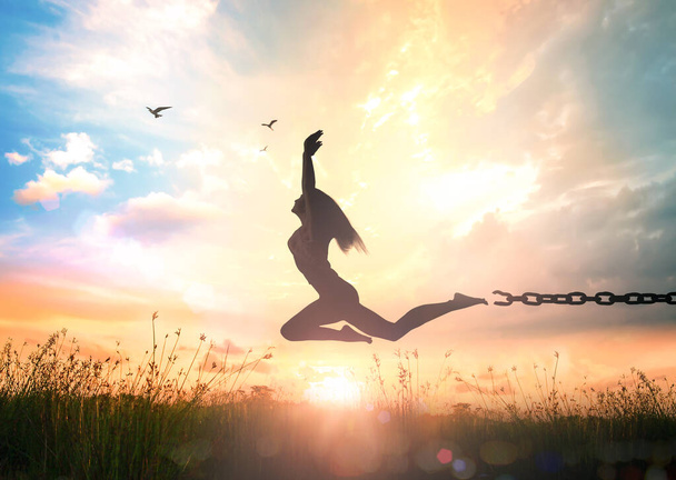 Международный день памяти работорговли и ее отмены: Силуэт девушки, прыгающей и разрывающей цепи на осеннем лугу заката с поднятыми руками - Фото, изображение