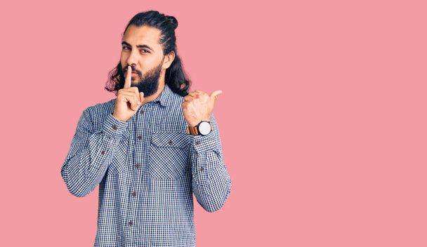 Young arab man wearing casual clothes asking to be quiet with finger on lips pointing with hand to the side. silence and secret concept.  - Foto, Bild