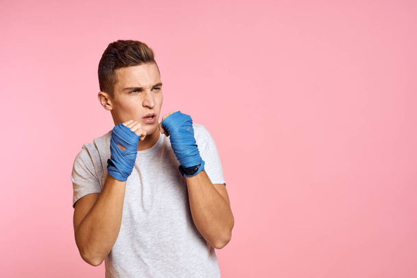 Guy in blue gloves on a pink background are boxing in a white t-shirt cropped view - Foto, afbeelding