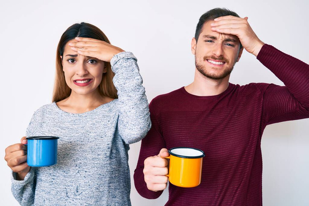 Beautiful couple holding coffee stressed and frustrated with hand on head, surprised and angry face  - Photo, Image