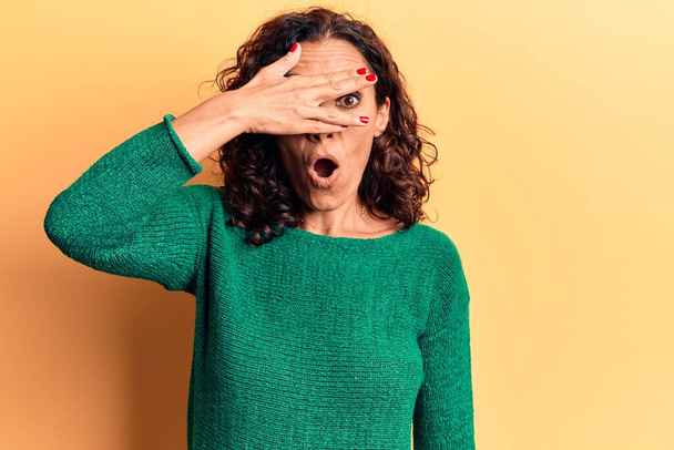 Middelbare leeftijd mooie vrouw dragen casual trui gluren in shock bedekking gezicht en ogen met de hand, kijken door vingers bang  - Foto, afbeelding