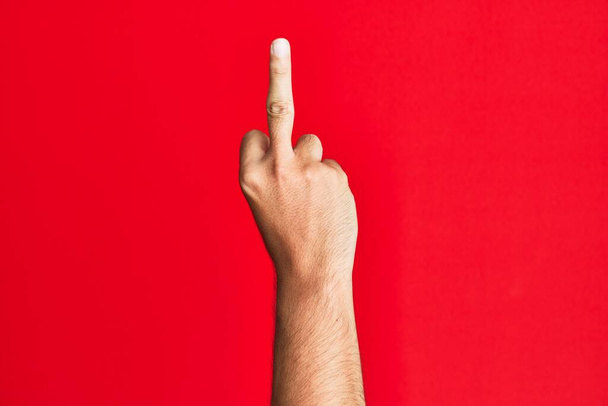 Рука білого білого чоловіка над червоним ізольованим тлом, що показує провокаційний і грубий жест, який робить хуй ви символ середнім пальцем
  - Фото, зображення