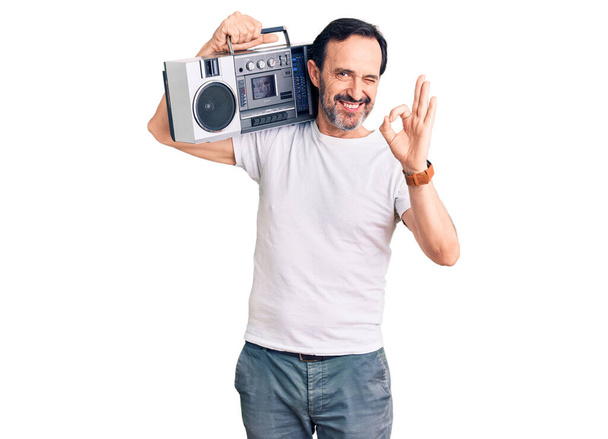 Middle age handsome man listening to music using vintage boombox doing ok sign with fingers, smiling friendly gesturing excellent symbol  - Foto, afbeelding