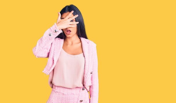 Young beautiful latin girl wearing business clothes peeking in shock covering face and eyes with hand, looking through fingers with embarrassed expression.  - Photo, Image