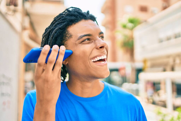 Young african american man smiling happy listening audio message using smartphone at street of city. - Zdjęcie, obraz