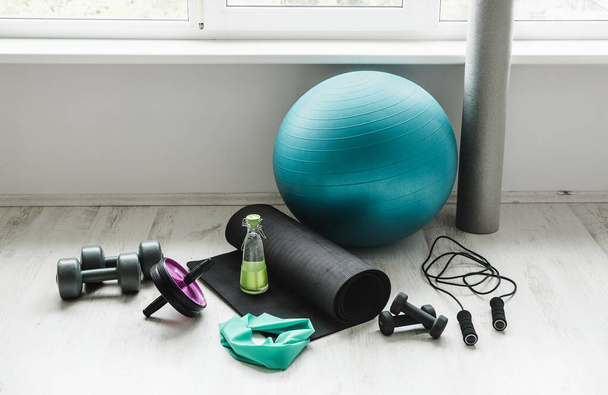 Group of different exercising equipment on white home gym floor. Fitness ball, round foam roller, resistance exercise latex band, jumping rope, dumbbells, yoga mat. Fit lifestyle concept. - Zdjęcie, obraz