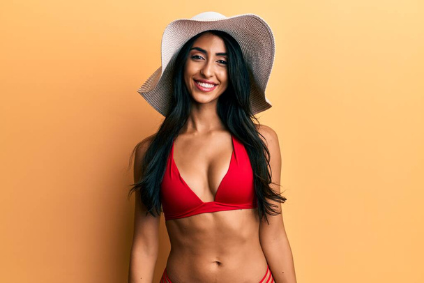Güzel İspanyol bir kadın bikini giyiyor ve yüzünde mutlu ve havalı bir gülümsemeyle yaz şapkası takıyor. şanslı kişi.  - Fotoğraf, Görsel