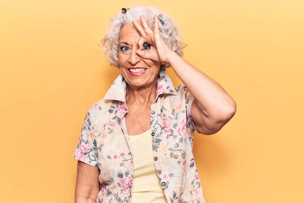 Femme âgée aux cheveux gris portant des vêtements décontractés souriant heureux faisant signe ok avec la main sur les yeux regardant à travers les doigts  - Photo, image