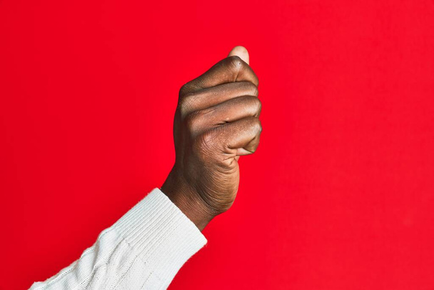 Bras et main de jeune homme noir afro-américain sur fond rouge isolé tenant l'espace vide avec pouce doigt, entreprise et publicité  - Photo, image