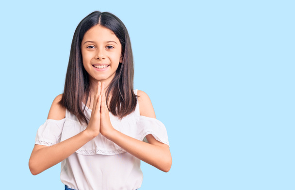 Krásné dítě dívka na sobě ležérní oblečení modlí s rukama dohromady prosí o odpuštění s úsměvem sebevědomí.  - Fotografie, Obrázek