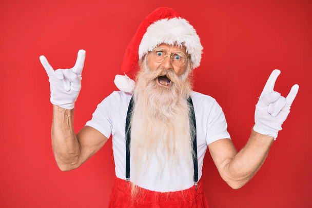 Old senior man with grey hair and long beard wearing white t-shirt and santa claus costume shouting with crazy expression doing rock symbol with hands up. music star. heavy concept.  - Fotó, kép