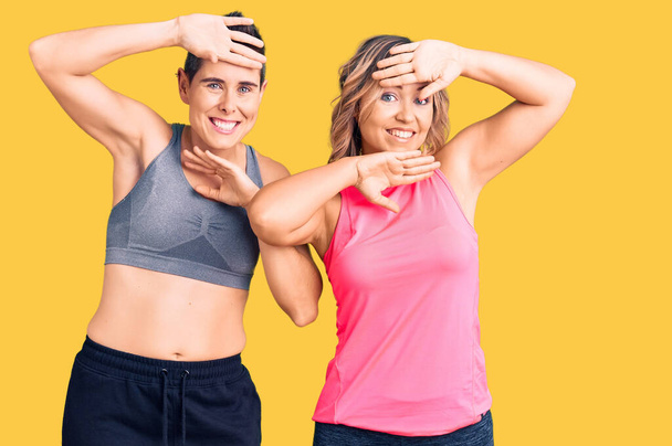 Couple of women wearing sportswear smiling cheerful playing peek a boo with hands showing face. surprised and exited  - Photo, Image