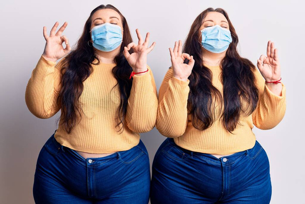 Young plus size twins wearing medical mask relax and smiling with eyes closed doing meditation gesture with fingers. yoga concept.  - Photo, Image