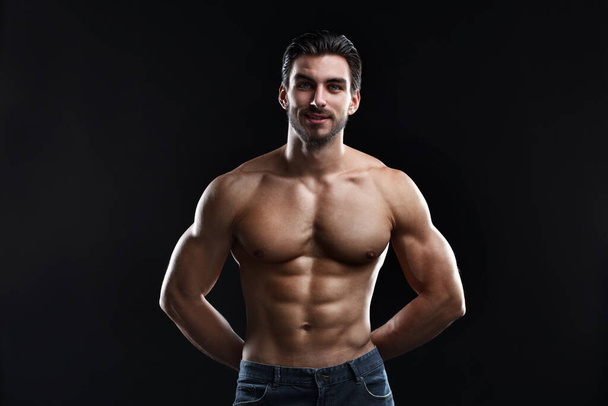 Young athletic man with a naked torso isolated on a black background. - Foto, afbeelding