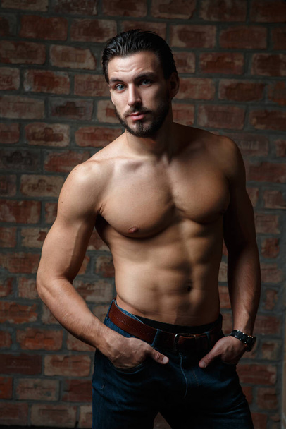 Young attractive athletic guy with a naked torso on a background of a brick wall. - Foto, Imagem