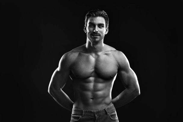 Black-white portrait of a young athletic man with a naked torso isolated on a black background. - Foto, Imagem