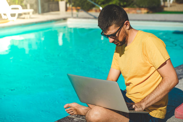 Young business man working with laptop on beautiful scenic mountain background. Business man working near swimming pool in a rural hotel. Freelancer. Traveler.  - Fotó, kép