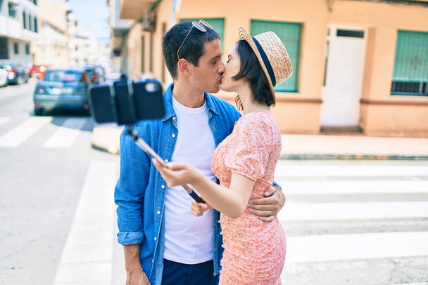 Красивая пара целуется делая селфи на смартфоне на улице города - Фото, изображение