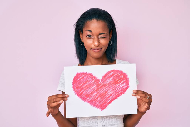 Genç Afro-Amerikalı bir kadın kalp krizi geçiriyor ve kameraya seksi bir ifadeyle, neşeli ve mutlu bir yüzle bakıyor..  - Fotoğraf, Görsel