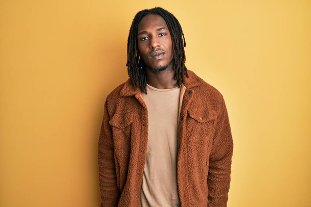 African american man with braids wearing brown retro jacket looking sleepy and tired, exhausted for fatigue and hangover, lazy eyes in the morning.  - 写真・画像