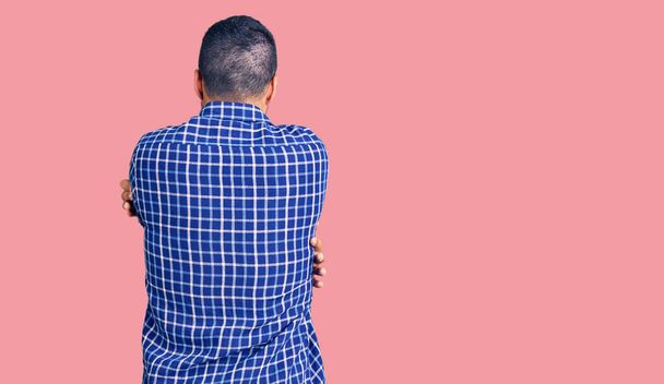 Jeune homme hispanique portant des vêtements décontractés s'embrassant heureux et positif à partir de l'arrière. amour de soi et soins de soi  - Photo, image