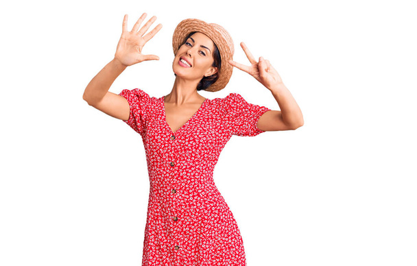 Молодая красивая женщина в летней шляпе показывает и указывает пальцами номер семь, улыбаясь уверенно и счастливо.  - Фото, изображение