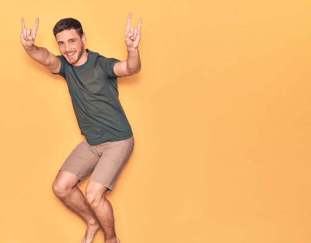 Young handsome hispanic man wearing casual clothes smiling happy. Jumping with smile on face doing horns sign with fingers over isolated yellow background - Foto, Bild