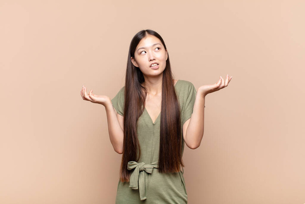 asian young woman shrugging with a dumb, crazy, confused, puzzled expression, feeling annoyed and clueless - Fotó, kép