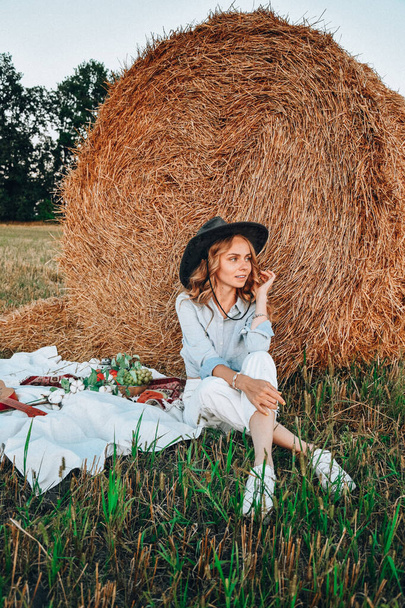 Piknik heinäparvella. Nainen cowboy-hatussa olkipaalin lähellä. Kesä, kauneus, muoti, glamour, elämäntapa käsite. Cottagecore maatilan luonnon. Pastoraalinen elämä - Valokuva, kuva