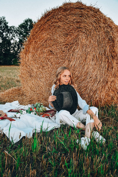 Picnic at the hayloft. Woman in cowboy hat sitting near a straw bale. Summer, beauty, fashion, glamour, lifestyle concept. Cottagecore farmcore naturecore. Pastoral life - Photo, Image