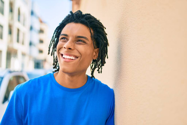 若いアフリカ系アメリカ人の男が笑顔で街の壁に寄りかかって. - 写真・画像