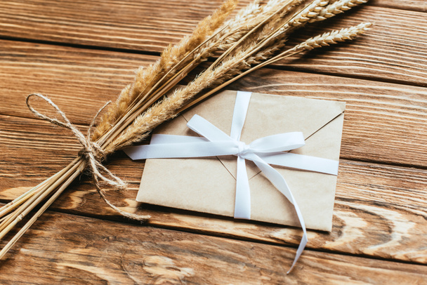 envelope with bow near wheat ears on wooden background - Photo, Image