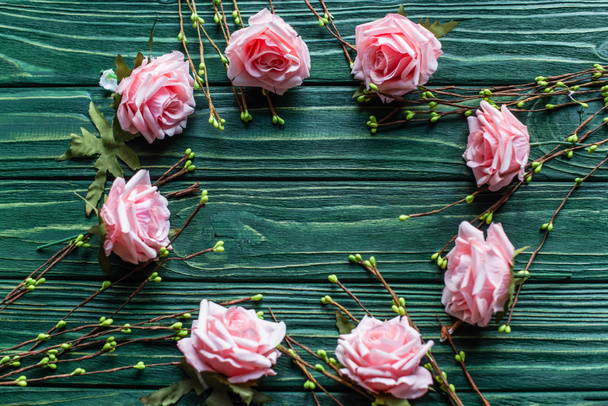 bovenaanzicht van houten groene achtergrond met bloeiende takken, rozen - Foto, afbeelding