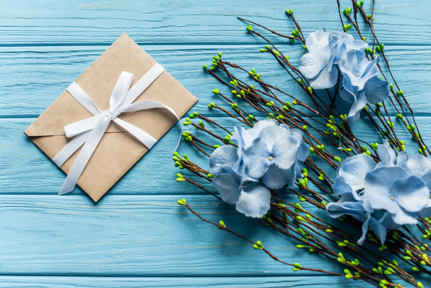 top view of wooden blue background with blossoming branches and flowers near envelope - Foto, Imagem