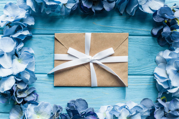 вид сверху на деревянный синий фон с цветочной рамкой вокруг конверта - Фото, изображение