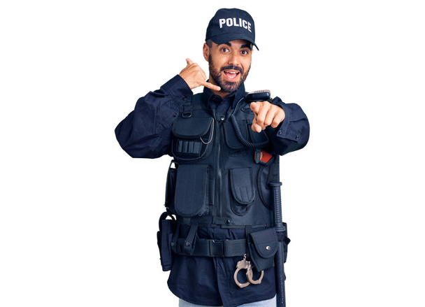 警察の制服を着た若いヒスパニック系の男が電話のジェスチャーで話をし、あなたを指して笑っています。電話してくれ.  - 写真・画像
