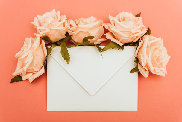 top view of white envelope and roses on coral background - Photo, Image