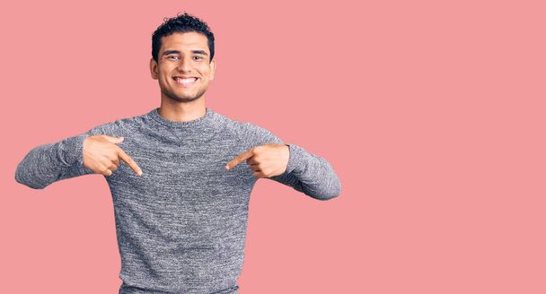 Латиноамериканец красивый молодой человек в обычном свитере выглядит уверенно с улыбкой на лице, указывая на себя пальцами гордым и счастливым.  - Фото, изображение