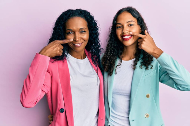 African american mother and daughter wearing business style pointing with hand finger to face and nose, smiling cheerful. beauty concept  - 写真・画像