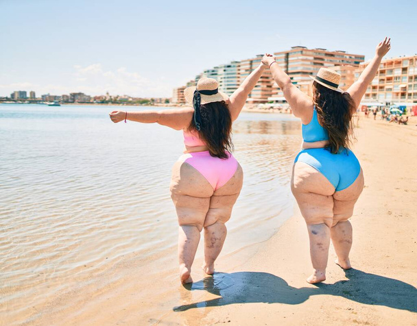 Two plus size overweight sisters twins women happy and proud of their bodies walking at the beach on summer holidays - Photo, Image