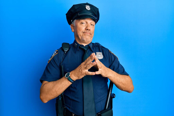 Όμορφος μεσήλικας ώριμος άντρας που φοράει αστυνομική στολή με τα χέρια ενωμένα και τα δάχτυλα σταυρωμένα χαμογελώντας χαλαρός και χαρούμενος. επιτυχία και αισιοδοξία  - Φωτογραφία, εικόνα