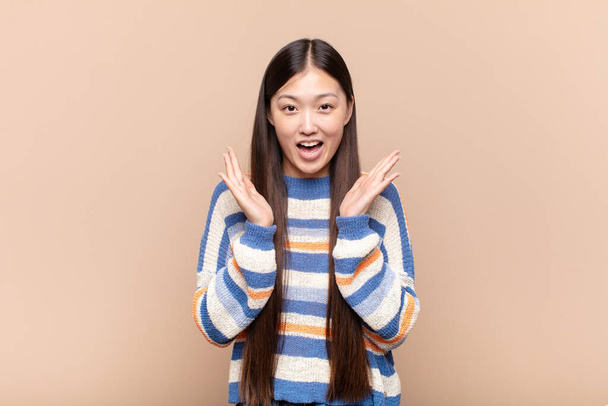 asian young woman looking happy and excited, shocked with an unexpected surprise with both hands open next to face - Фото, изображение