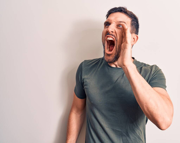 Young handsome man wearing casual t-shirt standing over isolated white background shouting and screaming loud to side with hand on mouth. Communication concept. - Photo, Image