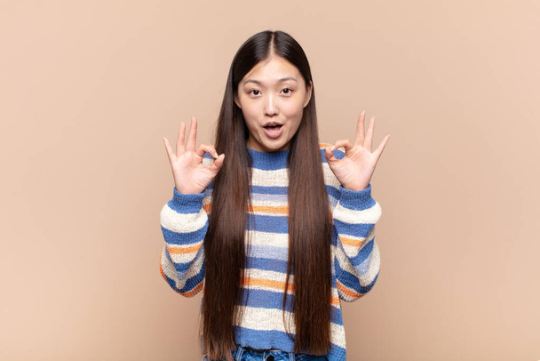 asian young woman feeling shocked, amazed and surprised, showing approval making okay sign with both hands - Foto, afbeelding